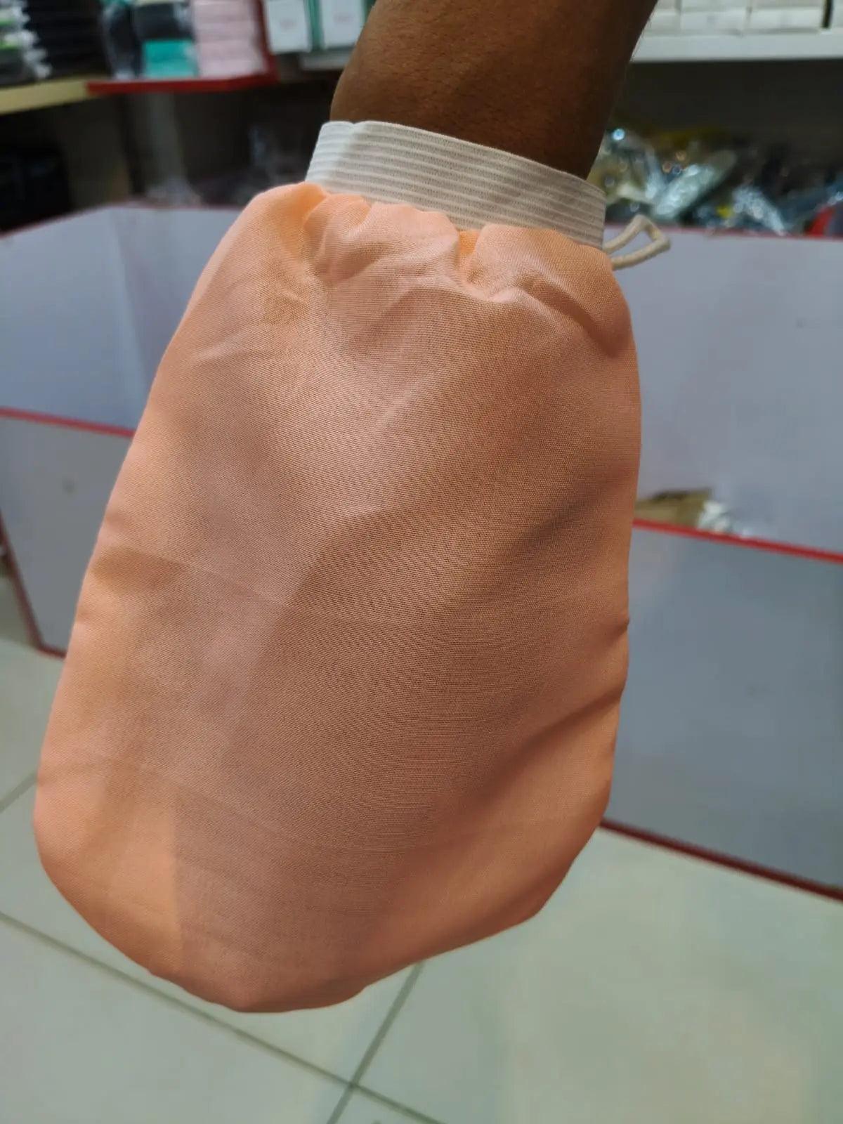 Peach-colored exfoliating bath scrub glove with an elastic wrist cuff, shown worn on a hand.