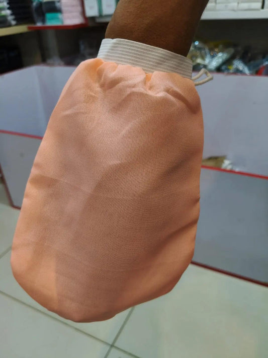 Peach-colored exfoliating bath scrub glove with an elastic wrist cuff, shown worn on a hand.